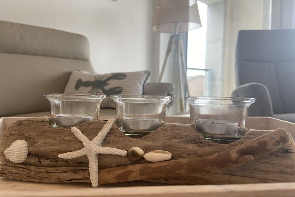 Un plateau en bois avec quatre verres à liqueur et une décoration en forme d’étoile de mer, posé sur une table dans une pièce où l’on aperçoit un canapé et une lampe au fond.