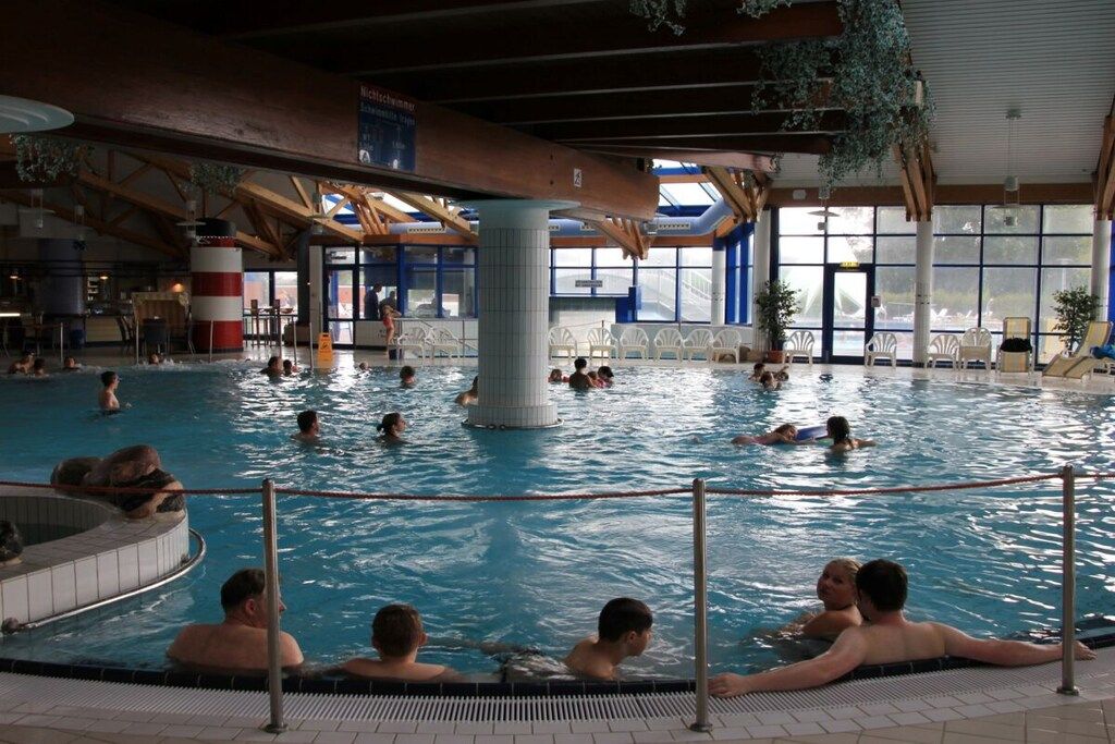 An indoor swimming pool with multiple lanes, a central column, and a view of the outside through large windows.