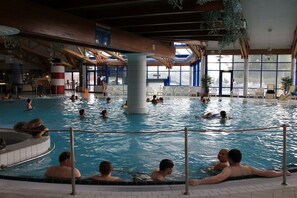 Ein Hallenbad mit mehreren Bahnen, einer zentralen Säule und Blick ins Freie durch große Fenster.