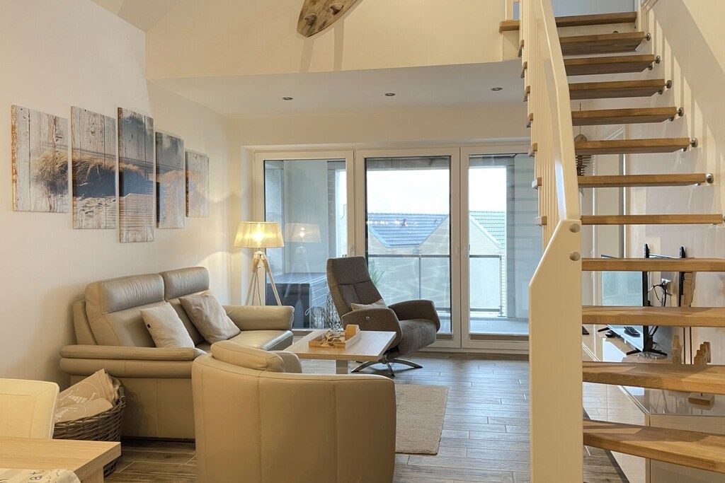 A modern living room with a sofa, armchair, and a coffee table. There is a staircase with wooden steps leading to an upper floor.