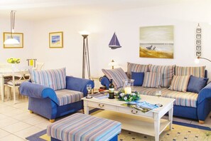 A living room with striped sofas, a coffee table, and a painting of a beach scene. - Holiday apartment with 1 bedroom (Lindaunis)