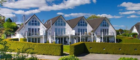 A row of white houses with gabled roofs, surrounded by well-maintained hedges and a clear sky.