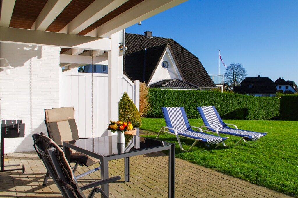 Une terrasse extérieure avec une table et des chaises, un petit jardin et une maison en arrière-plan.