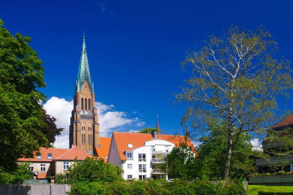 A church with a tall spire and a modern building with balconies.