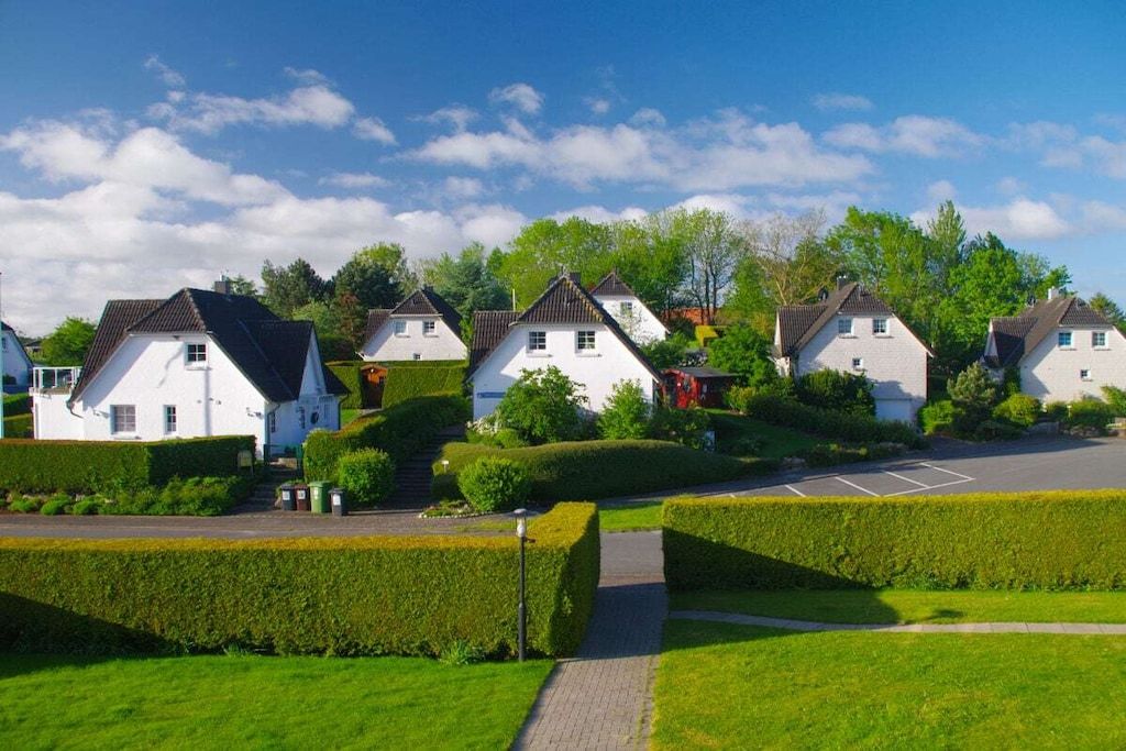A residential area with white houses, a paved driveway, and well-maintained hedges.