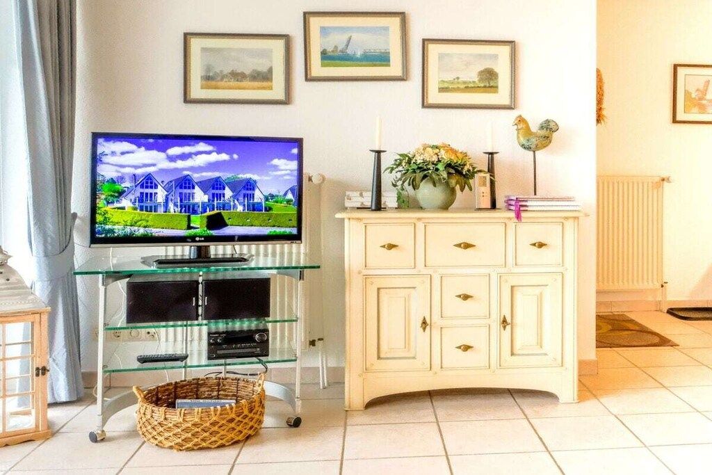 A living room with a television on a glass stand, a white cabinet with drawers, and framed pictures on the wall.
