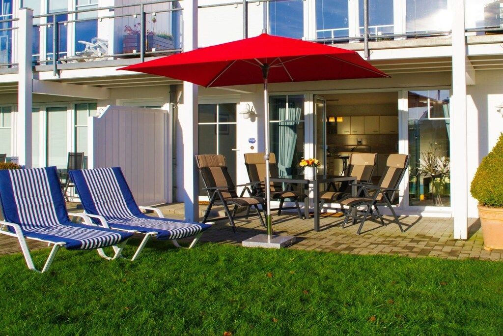 A patio with outdoor seating, including lounge chairs and a table with chairs, under a red umbrella.