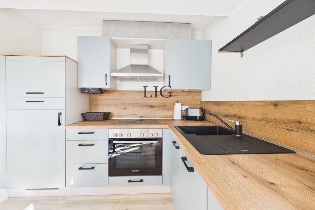 Eine moderne Küche mit weißen Schränken, einer Holz Arbeitsplatte, einem Bosch-Ofen und einem Spülbecken.