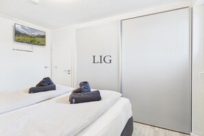 A hotel room with two beds, a flat-screen TV mounted on the wall, and a door with the text 'LIG' on it. - Holiday apartment Dünengras (Langeoog)