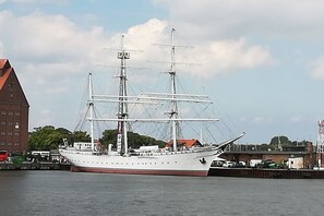 Un barco blanco grande amarrado en un puerto, con un edificio rojo al fondo.