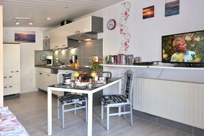 Cozinha moderna com área de refeições, televisão e estante de livros.