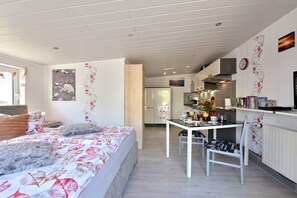 Ein Schlafzimmer mit einem Bett, einem Nachttisch und einem Fenster. Es gibt eine Küchenzeile mit einem Herd, einer Spüle und einem Kühlschrank.