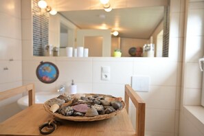 Een badkamer met een houten tafeltje, een mand met stenen en een spiegel die de ruimte weerspiegelt.