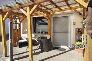 A covered patio area with a wooden pergola, outdoor seating, and a door leading to a garage. - Studio "My Relaxation Kingdom" (Garz auf Rügen)