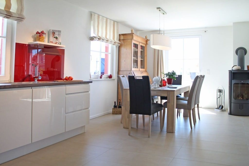 Una cocina moderna con armarios blancos, una zona de comedor con mesa y sillas de madera, y una estufa empotrada.