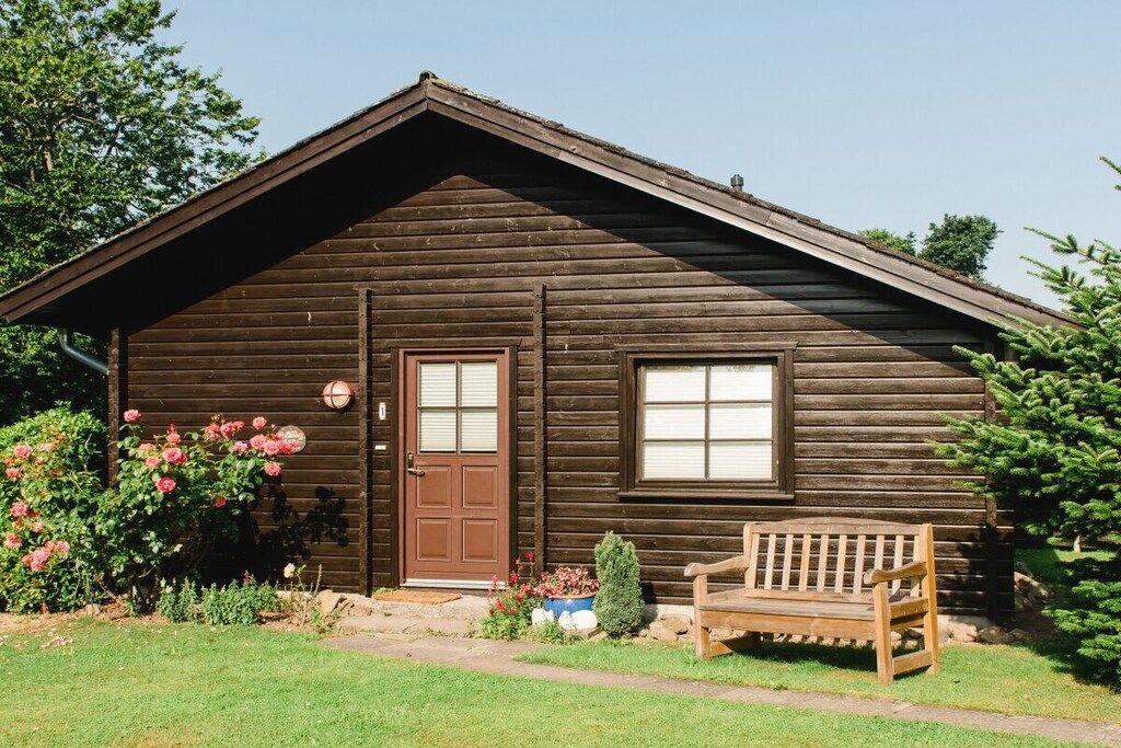A wooden cabin with a front door, a window, and a bench outside.