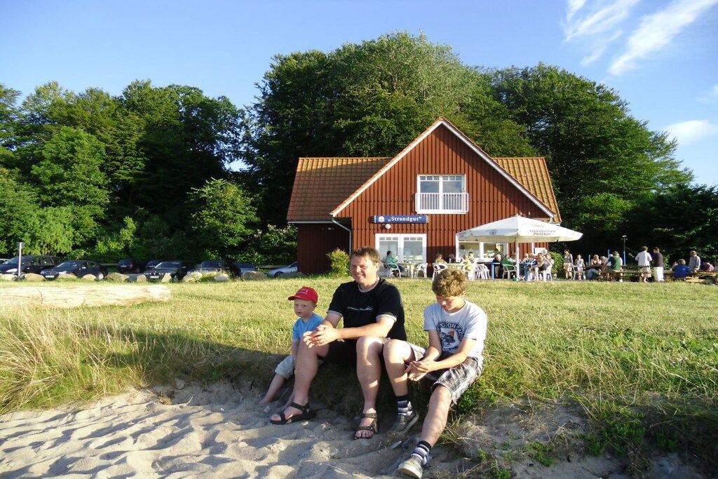 Une famille est assise sur une étendue de sable, avec un bâtiment rouge en arrière-plan.