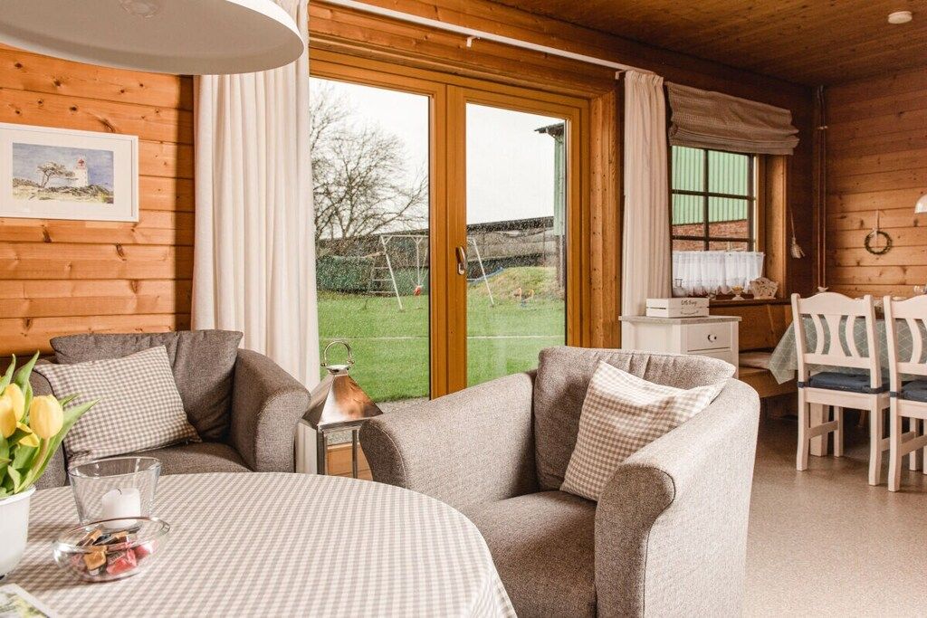 A cozy room with a sofa, a small table with a checkered tablecloth, and a view of a green outdoor area through a glass door.