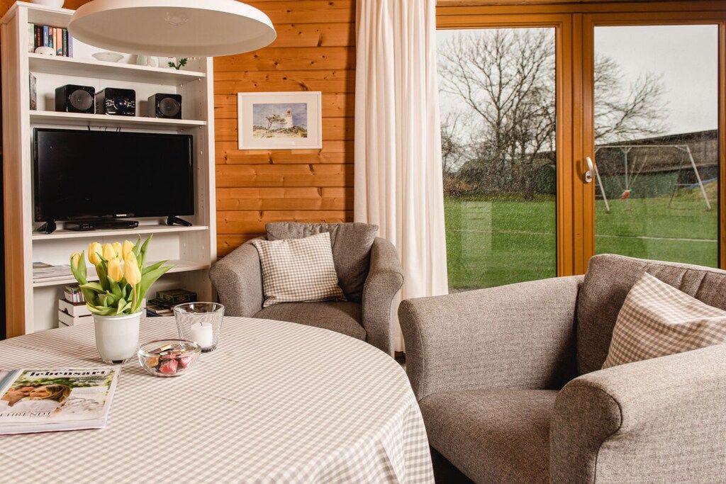Een gezellige woonkamer met een televisie, een boekenkast, een tafel met een tijdschrift en uitzicht op de omgeving.