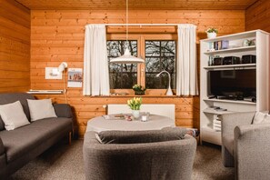 A cozy cabin interior with a sofa, armchair, and a small table with flowers. - Struve 1 on the Kastanienhof (Quern)