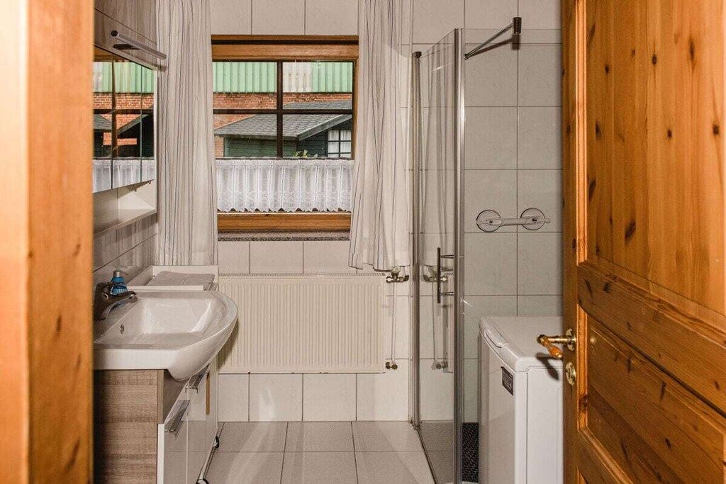 A compact bathroom with a sink, a window with a view of buildings, a shower, and a wooden door.