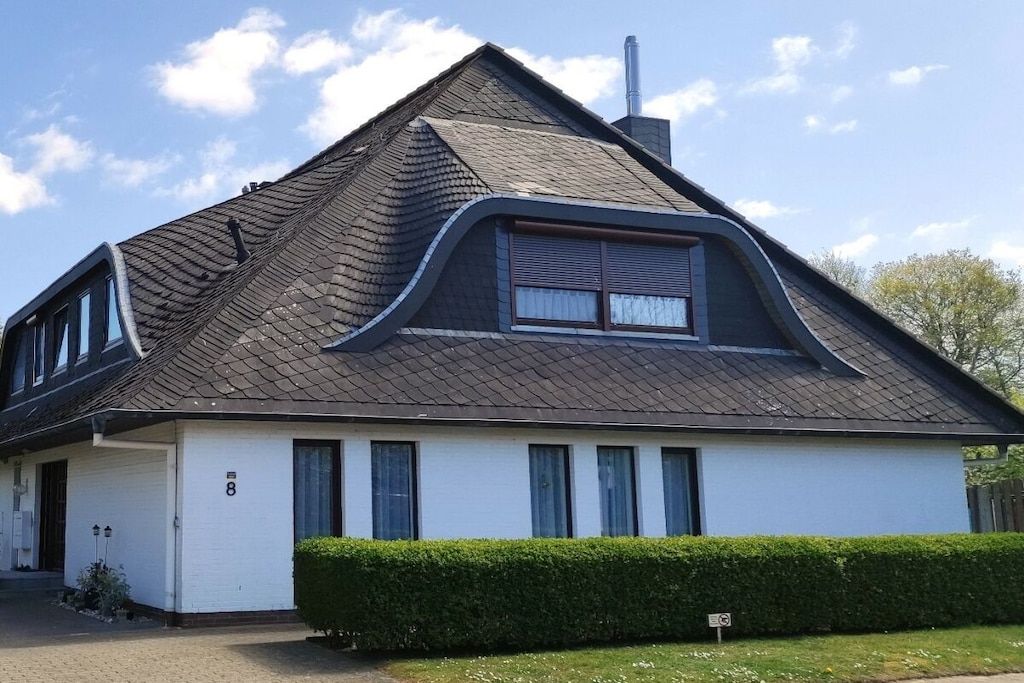 Een gelijkvloers huis met een puntige daken, een garage en een verzorgde haag.
