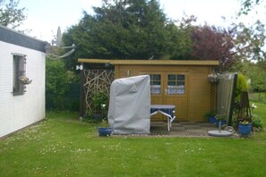 A small wooden shed with a covered table and chairs, a satellite dish, and potted plants. - Holiday apartment with 2 bedrooms (Büsumer Deichhausen)