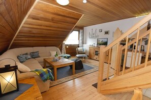 Un espacio habitable estilo loft acogedor, con techo de madera, un sofá, una mesa de centro, un televisor y una escalera.