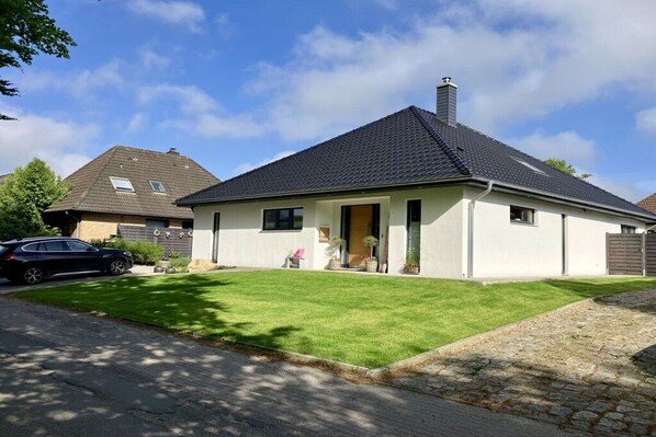 Ein einstöckiges Haus mit Satteldach, befestigter Auffahrt und gepflegtem Rasen.