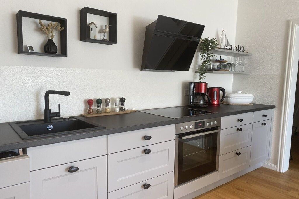 Una cocina moderna con horno integrado, extractor de aire negro y encimera con lavabo.