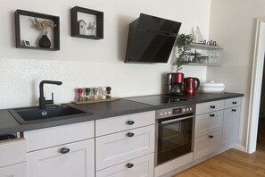 A modern kitchen with a built-in oven, a black range hood, and a countertop with a sink. - Holiday apartment in Hürup with swimming pool (Hürup)