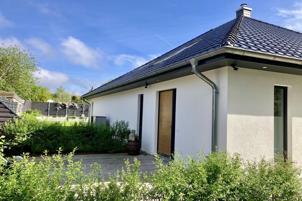 A modern house with a sloped roof, a front door, and a small garden area.