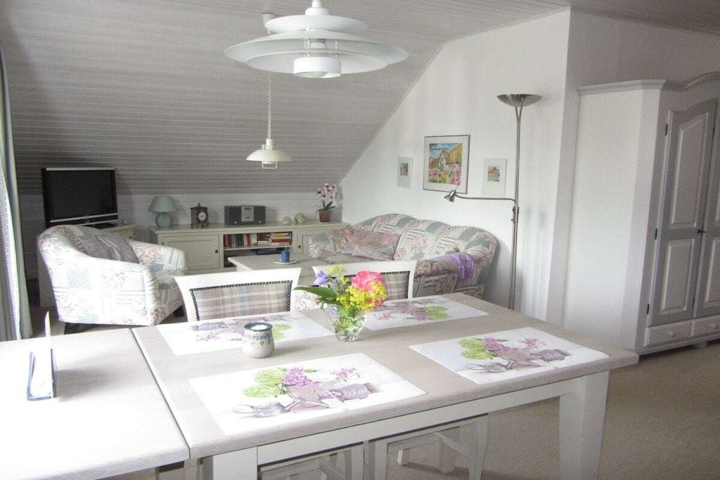 A room with a dining table, chairs, a television, a sofa, and a cabinet.