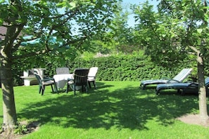 A garden with a table and chairs, a hedge, and a tree. - Holiday apartment with 2 bedrooms (Malente OT Timmdorf)
