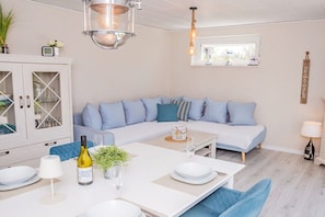 Een moderne woonkamer met een modulaire bank, een eettafel gedekt voor twee personen en een kast met glazen deuren.