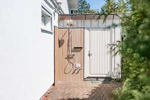 A white building with a wooden gate and a white door, a metal railing, and a brick pathway. - House Sansibar Niendorf (Timmendorfer Strand)