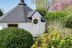 A white building with a dark roof, surrounded by dense green foliage and flowering plants. - House Sansibar Niendorf (Timmendorfer Strand)