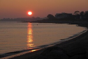 A sunset over a calm body of water with a beach in the foreground. - House Sansibar Niendorf (Timmendorfer Strand)