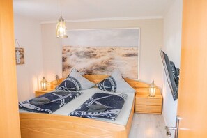 A bedroom with a bed, bedside lamps, a wall-mounted TV, and a large abstract painting. - House Sansibar Niendorf (Timmendorfer Strand)