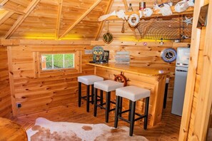 A wooden cabin interior with a bar area, stools, a window, and a refrigerator. - House Sansibar Niendorf (Timmendorfer Strand)
