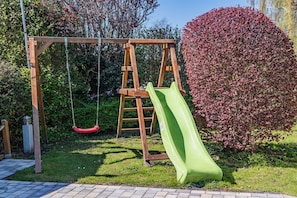 A wooden swing set with a green slide in a garden. - House Sansibar Niendorf (Timmendorfer Strand)