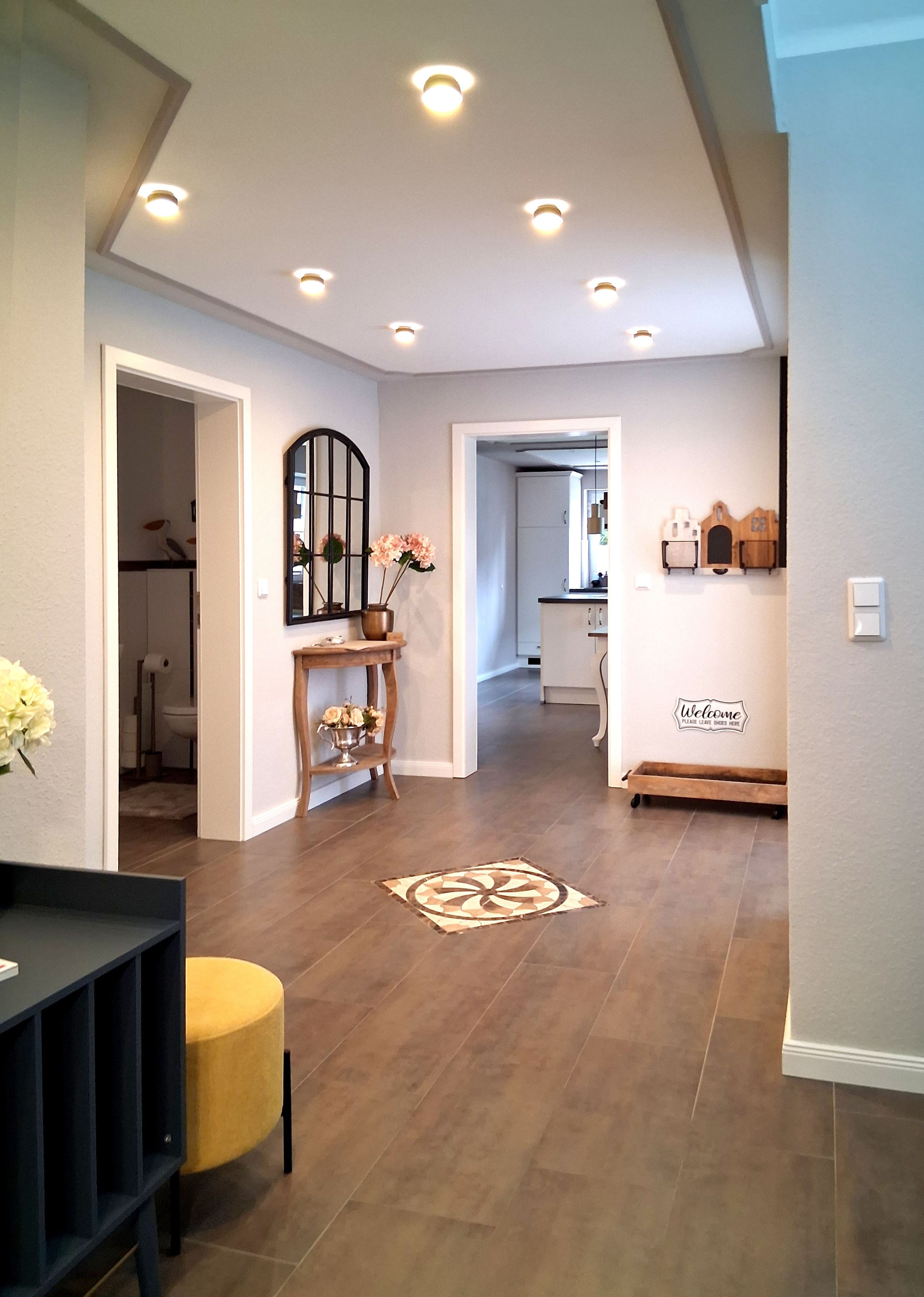 Un intérieur moderne avec un couloir central, des spots encastrés au plafond, un tapis décoratif et un panneau d’accueil.