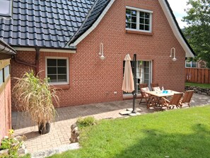 A brick house with a tiled roof, a patio with a table and chairs, and a potted plant. - Holiday Home 'Holidate-Inn' with Private Terrace, Private Garden and Wi-Fi (Stadum)