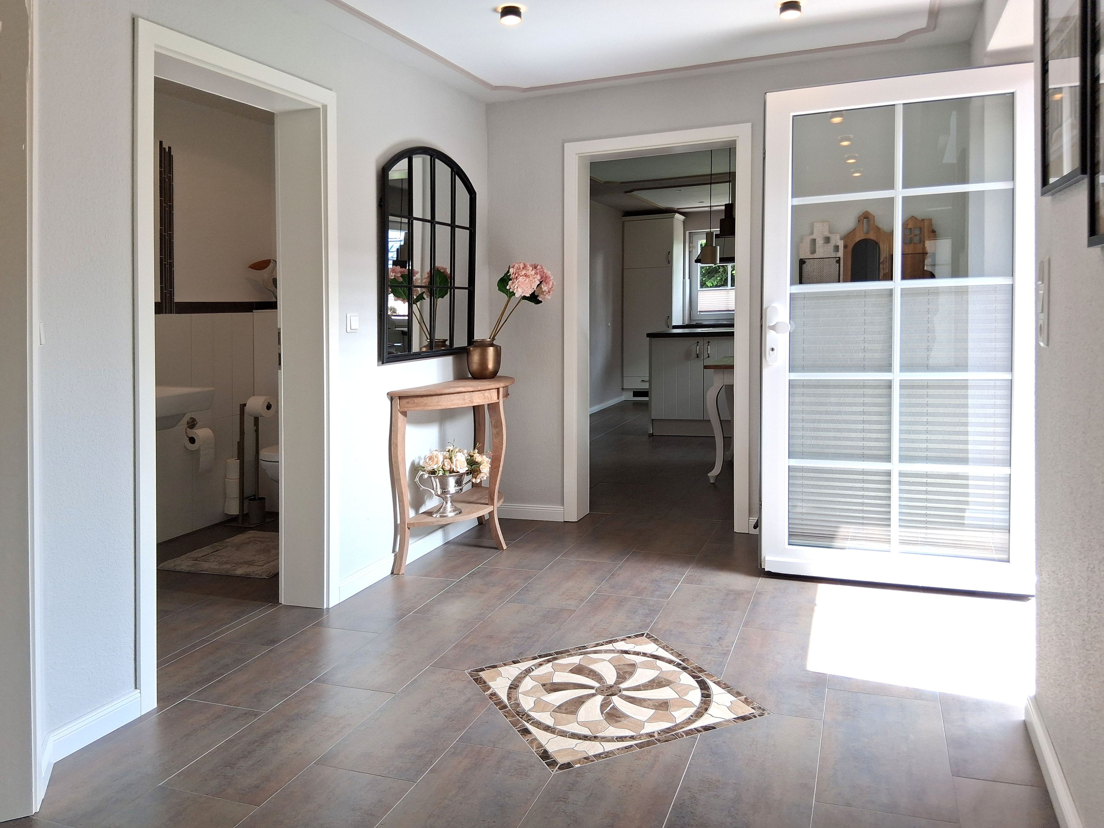 A hallway with a tiled floor, a decorative rug, a mirror, and a door leading to a kitchen area.