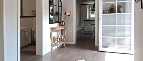 A hallway with a tiled floor, a decorative rug, a mirror, and a door leading to a kitchen area.
