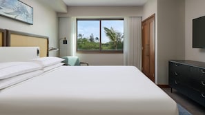Quarto de hotel com uma cama grande, uma escrivaninha, uma cadeira, um guarda-roupa e uma janela com vista para árvores.