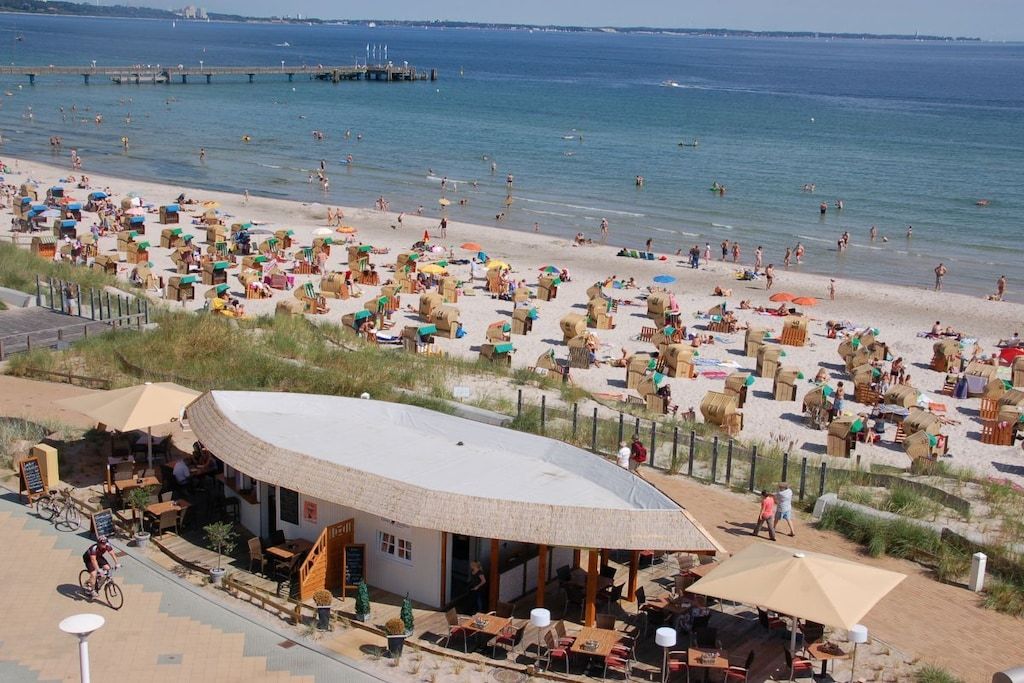 A beachside café with outdoor seating, a view of the beach, and a pier in the background.