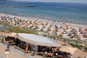 A beachside café with outdoor seating, a view of the beach, and a pier in the background. - Holiday apartment with 2 bedrooms (Scharbeutz)