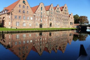 A historic building with a symmetrical facade, arched windows, and a red-tiled roof, reflected in a calm body of water. - Holiday apartment with 2 bedrooms (Scharbeutz)