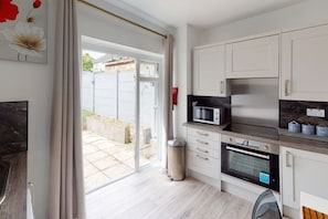 A modern kitchen with white cabinets, a microwave, an oven, and a sliding glass door leading to a patio area. - Apartment 101 - Symons House (Medway)